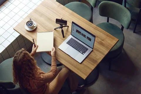 Woman writing notes while sitting at table with laptop Stock Photos