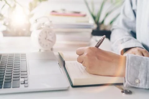 Woman is writing in planner notebook while using laptop to work or plan wit.. Stock Photos