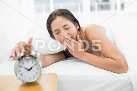 Woman yawning while extanding hand to alarm clock Stock Photos