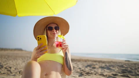Woman in a yellow bikini using a smartphone while enjoying a refreshing coc.. Stock Footage 341343503