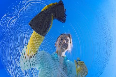 Woman in yellow gloves cleaning window glass with rag on a blue sky background Stock Photos