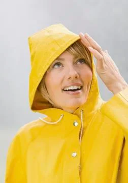 Woman in yellow rain coat looking up and smiling Stock Photos