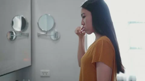 Woman in Yellow Top Examining Reflection in Bathroom Mirror Stock Footage 314994792