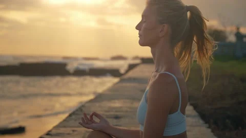 Woman in zen meditation sitting on yoga mat during sunset at coast, slowmo Stock Footage