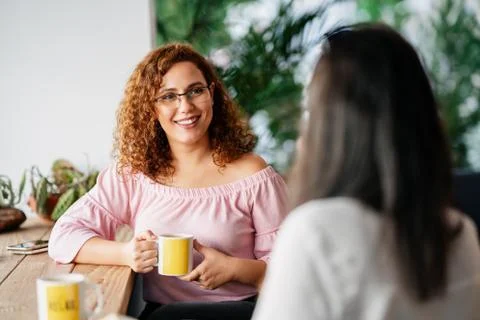 Womans chatting and smiling while they sitting and drinking some beverage in a Stock Photos