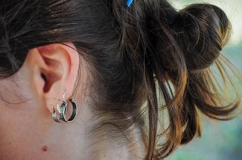 Woman's ear with multiple earrings, brown hair in messy bun, casual elegance. Stock-Fotos