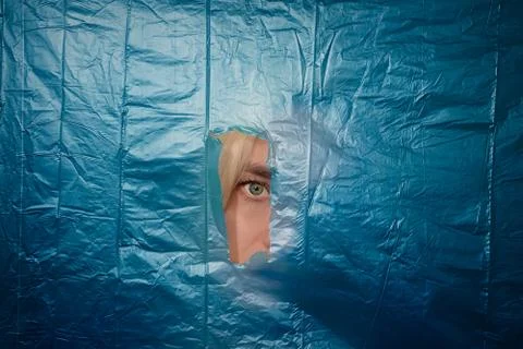 Woman's eye looking through torn off blue nylon barrier Stock Photos