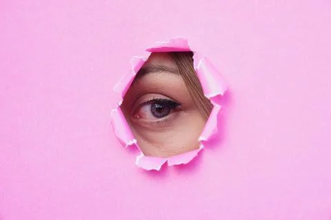 A woman's eye looking through torn pink paper. copy space for text Stock Photos