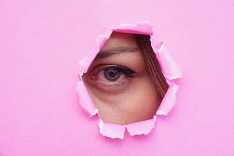 A woman's eye looking through torn pink paper. copy space for text Stock Photos