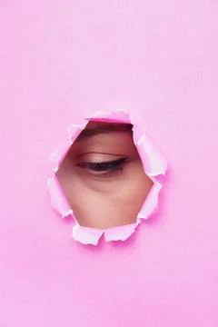 A woman's eye looking through torn pink paper. copy space for text Stock Photos
