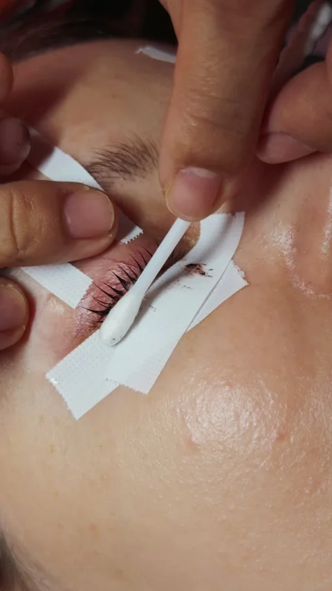 Woman's eye receiving lash extension procedure, white medical tape isolating Stock Footage 332815087