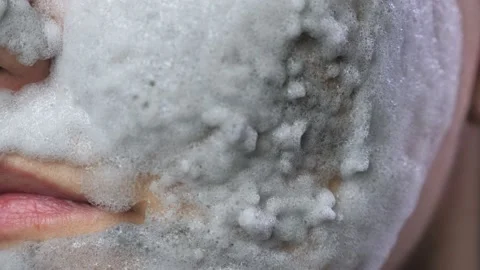 A woman's face with a gray bubble clay mask in a close-up. A girl applies a Stock Footage 232171047