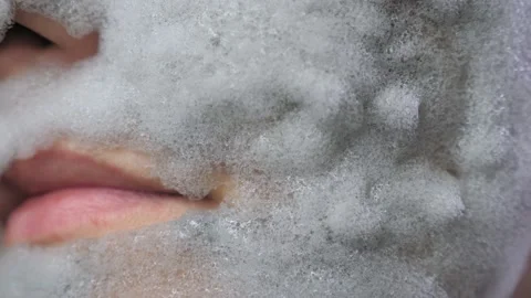 A woman's face with a gray bubble clay mask in a close-up. A girl applies a Stock Footage 232903548