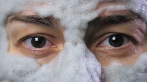 A woman's face with a gray bubble clay mask in a close-up. A girl applies a Stock Footage 233165382