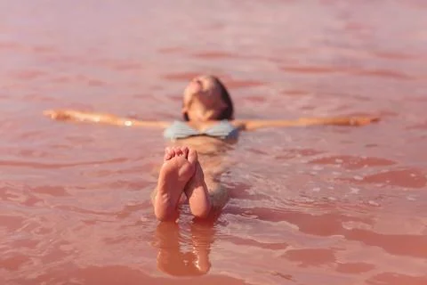 Woman's feet in focus while floating in pink lake Stock Photos