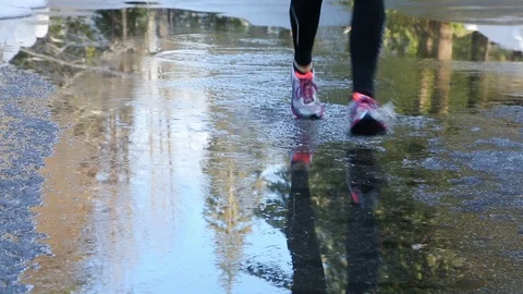 Woman's feet running through puddle. People exercising outdoors in wet weather. Stock Footage 107385997