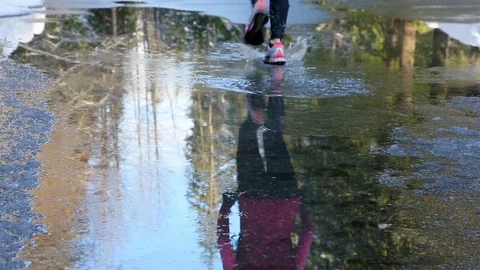 Woman's feet running through puddle. People exercising outdoors in wet weather. Stock Footage 107386049