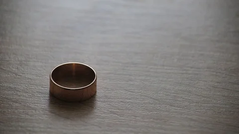 Woman's gold wedding ring rolling to man's one on a table Stock Footage 97955117