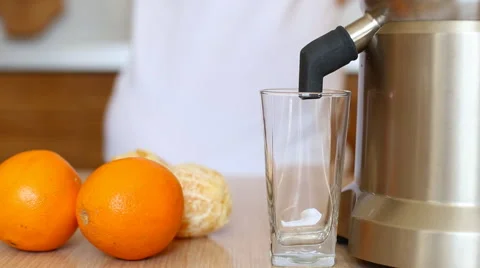 Woman's hand  adding carrot in juicer machine. Fresh orange juice pours of Stock Footage 61177312