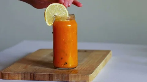 Woman's hand adding fruits in fresh orange smoothie on wooden board Video stock 70967476