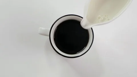 Woman's hand adding some milk to coffee in white cup on white table, top view Stock Footage 123337314