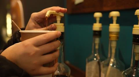 Womans hand adding syrup in ciffee. Hazel syrup for coffee. Nuts in coffee li Stock Photos