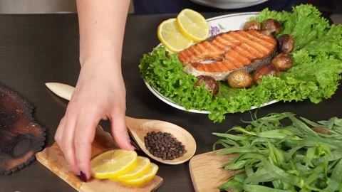 Woman's hand adds  slised  lemons on the fried salmon on the plate Stock Footage 143567785