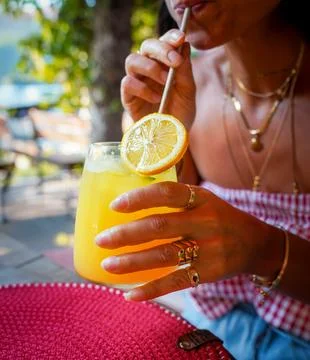 Woman's Hand Adjusting Lemon Slice on Fresh Orange Juice Cocktail Fotos Stock