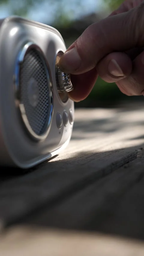 A woman's hand adjusts the volume on a portable smart speaker outdoors. Stock Footage 339976997