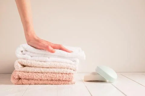 Woman's hand and a stack of soft towels with soap on a rustic table. The concept Stock Photos