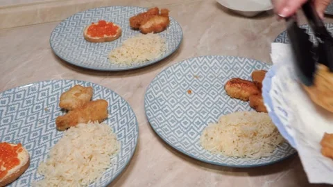 A woman's hand arranges batter-fried fish on plates on the kitchen table. Video stock 221151927