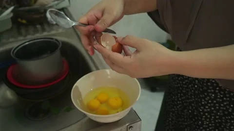 Woman's hand is beating eggs with a spoon and put in a bowl Stock Footage 221210605