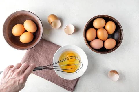 A woman's hand is beating eggs with a whisk on the kitchen table. Stock Photos