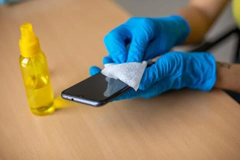 Woman's hand in blue gloves sanitizing cleaning smartphone mobile phone with  Stock Photos