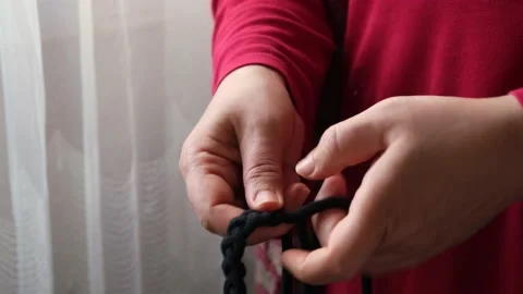 Woman's hand braiding with black threads. The woman who knits and creates a patt Stock Footage 145983979