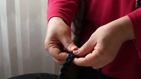 Woman's hand braiding with black threads. The woman who knits and creates a patt Stock Footage 145984034