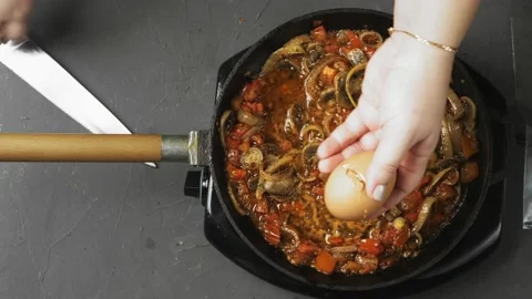 A woman's hand breaks an egg with a knife into a frying pan with shakshuka Stock Footage 170450851