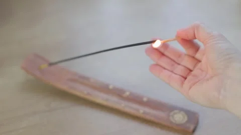 A womans hand with a burning match lights incense. Video stock 266898437