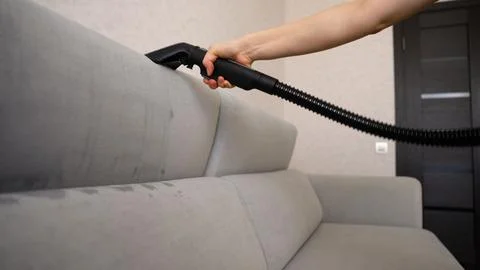 Womans hand cleaning grey sofa with professional extraction machine Stockfoto's
