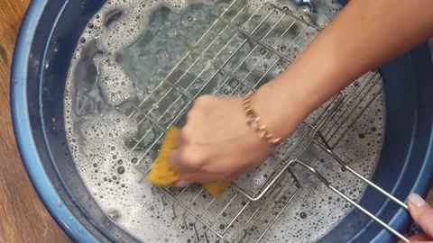 A womans hand cleans a grill grate with a sponge in soapy water, washing th.. Stock Footage 319441972