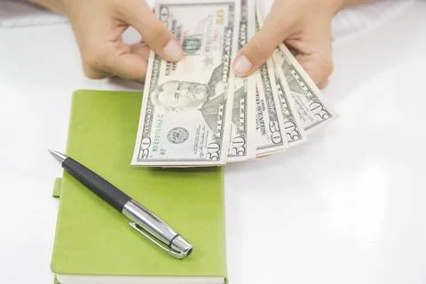 A woman's hand counting dollars, notebook and pen on the table Stock Photos