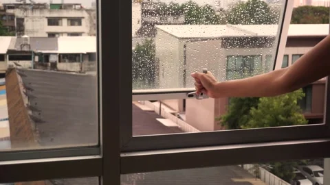 Woman's hand covering condo window, raindrops on the outside glass, roof of a ho Vidéo 180961731