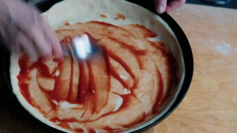 Woman's hand covers the dough with tomato sauce and stirs it with a spoon Stock Footage 297102779