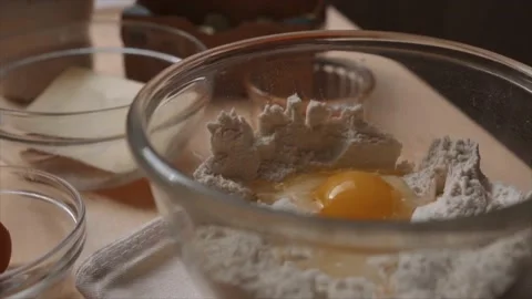 Woman's hand cracking and adding an egg into a bowl containing flour Stock Footage 229707299