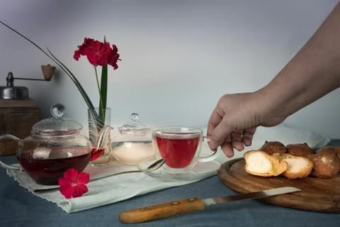 Woman's hand with a cup of tea on the table  , scones and geranium flower in Stock Photos