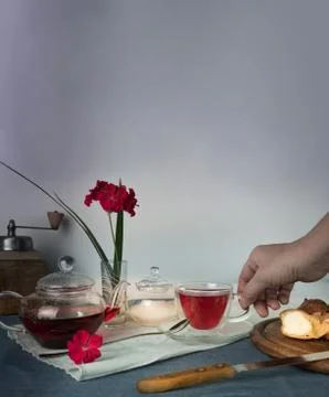 Woman's hand with a cup of tea on the table with tea, scones and geranium flower Stock Photos