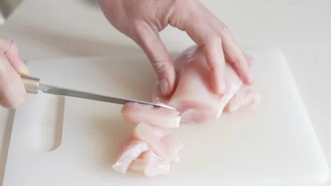 A woman's hand cuts a chicken fillet on a cutting board with a knife Stock Footage 234428083