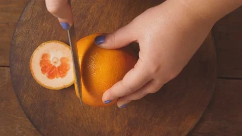 A woman's hand cuts a grapefruit into rings with a knife on a wooden board. Medi 库存影片 169409138