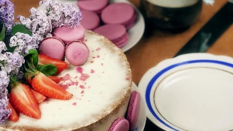 Woman's hand cuts off a piece of cake decorated with macaroons, strawberries and Video stock 99320833