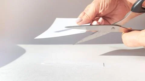 A woman's hand cuts a sheet of white paper with scissors and cuts off the cor Stock Photos
